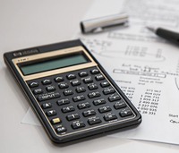 A calculator sits on a table with a pen and a financial report