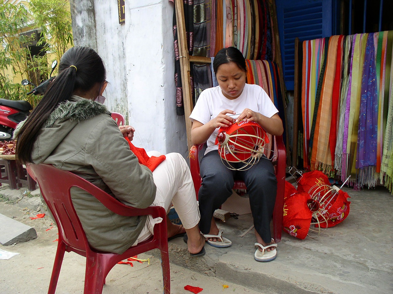 Two southeast Asian women sit in a hut constructing lanterns