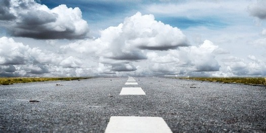 Photo of a straight empty road leading to a horizon stacked high with storm clouds