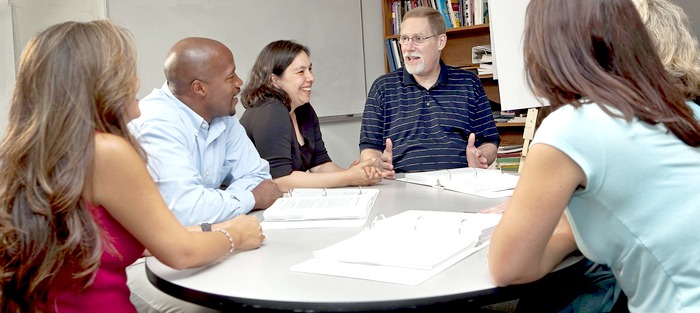 Several men and women of varied ages and races having a friendly discussion around a table in an office or classroom