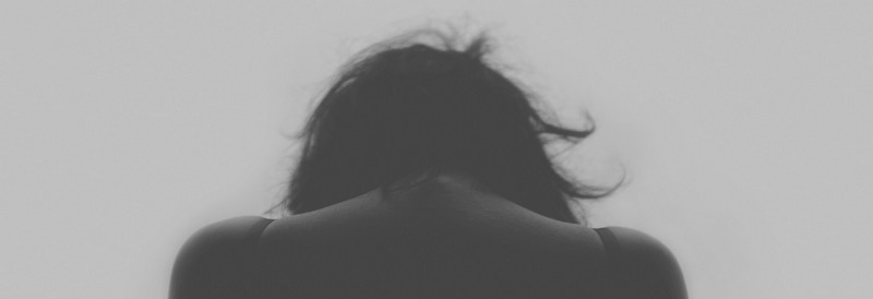 A picture from the back of a woman with her head bent forward In a featureless foggy space
