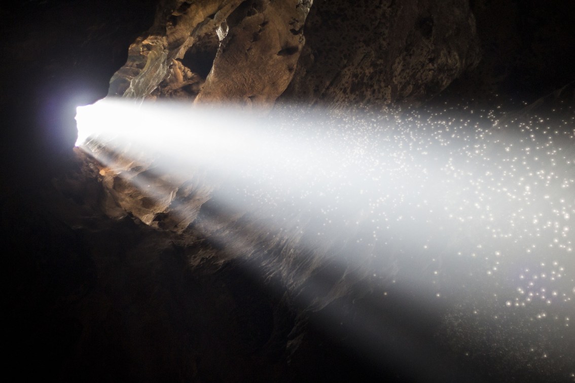 A bean of light shines into a cave through a hole at one side