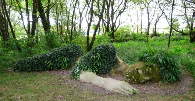 Image by Volker Lekies Plant-covered stone sculpture of woman sleeping stretched out on the ground as if she is halfway under the earth.