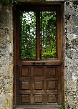 Leafy trees show through windows in a wooden door set in a stone wall.