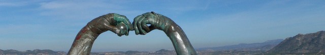 One giant bronze hand meets another, passing something round, against a backdrop of a mountain landscape