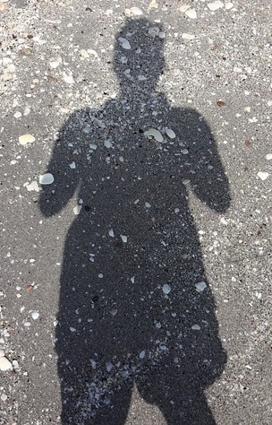 The shadow of a woman on a sandy beach strewn with stones