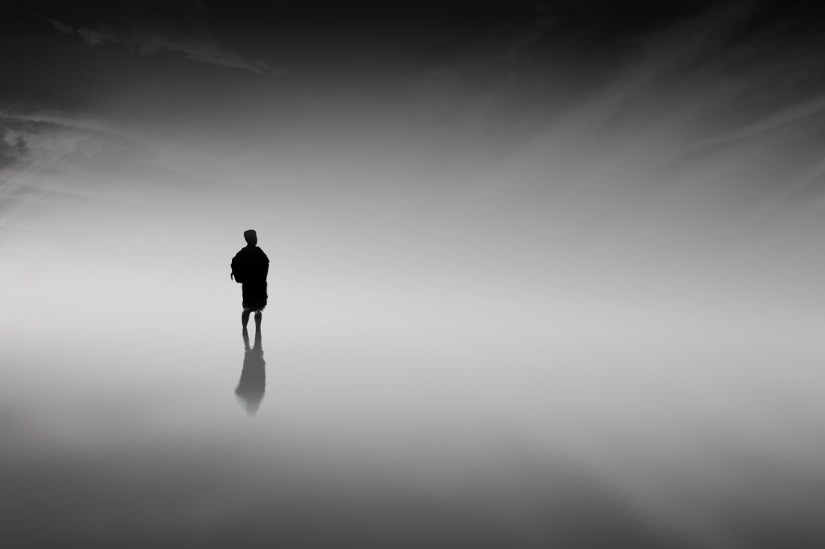 A silhouetted youth with a backpack in a completely featureless, misty space