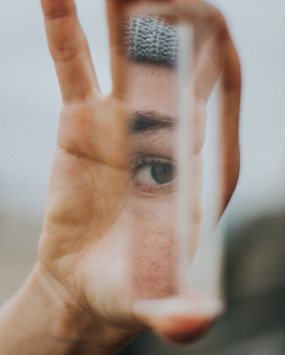 A hand holds up a thin strip of mirror, in which is reflected an eye and cheek