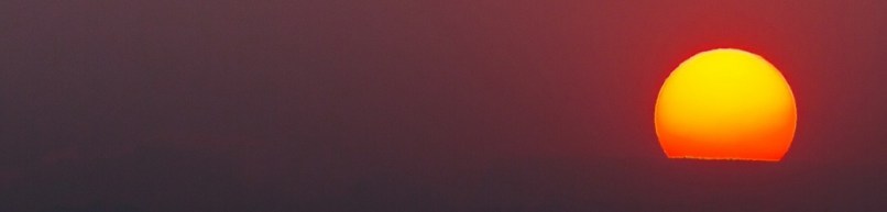 A huge yello sun sets at the dark horizon in a red sky.