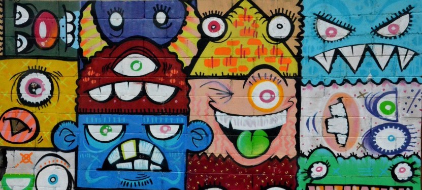 A grid of brightly colored, grotesque faces painted on a wall.