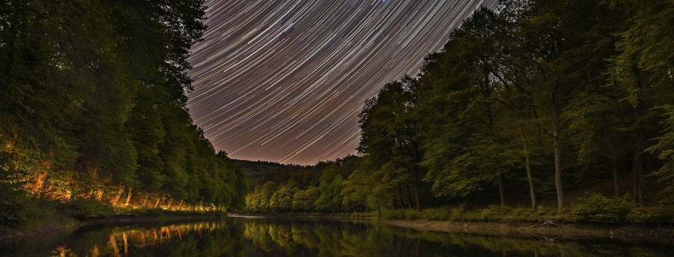Time lapse star streaks over a forest pond